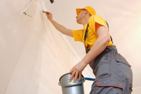 Builder priming wall using a brush in new apartment. Preparation of walls for painting or wallpapering. Home restoration concept.