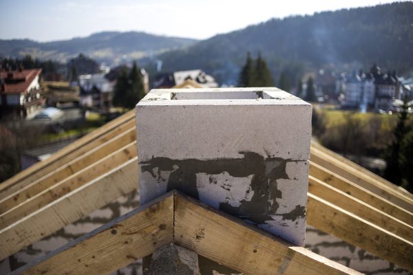 Close-up detail of roof frame of rough wooden lumber beams and chimney made of foam insulation blocks on blurred green background. Building, roofing, construction and renovation concept.