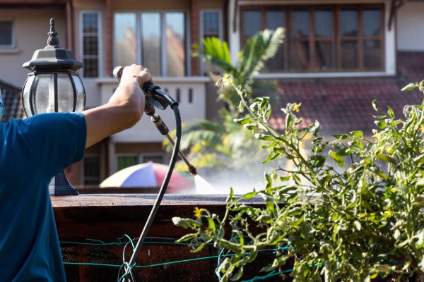 Worker using high pressure water jet spray gun to wash and clean dirty wall with moss at residential building in renovation